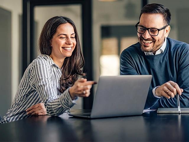 Zwei Personen diskutieren am Arbeitsplatz und schauen auf einen Laptop.