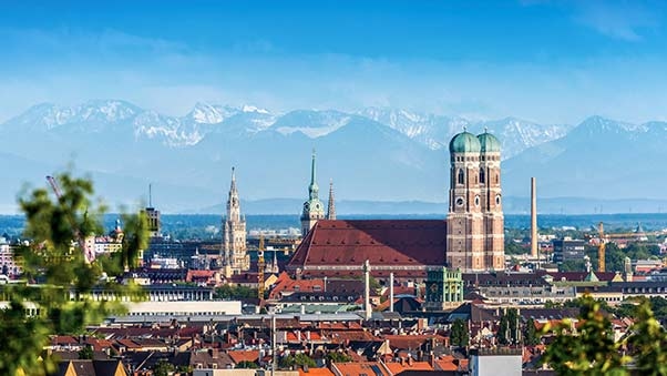 Blick auf die Skyline von München mit Frauenkirche und den Alpen im Hintergrund.